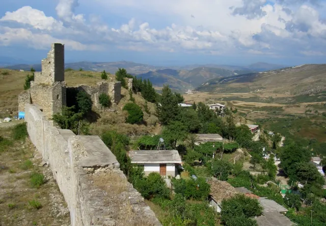 Ruined walls and a stone tower on a hill above an open valley with a few houses