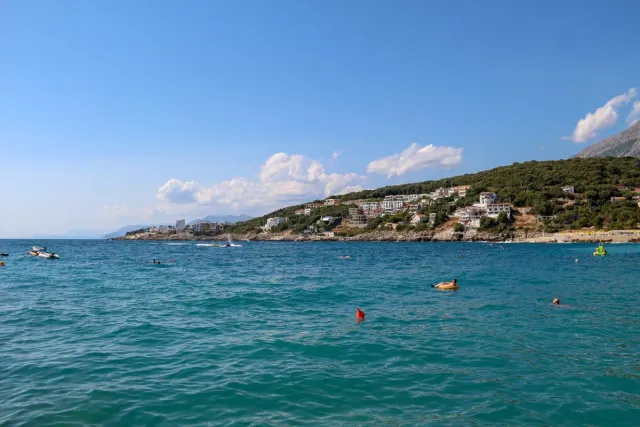 Turquoise water with bathers and floats, and a green slope with white houses behind