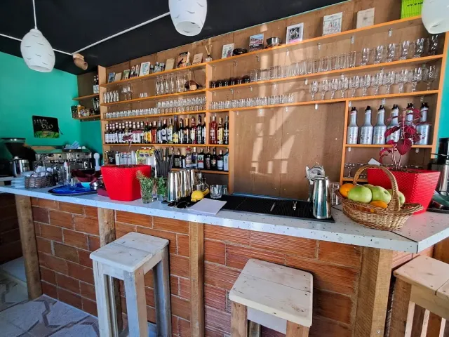A bar counter with a brick base, wooden stools and shelves loaded with glasses and bottles