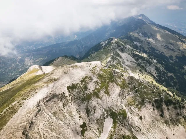 An aerial shot of a bare rocky ridge with patches of green, and low clouds on the peaks