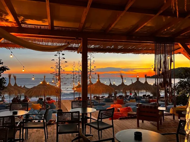 A beach bar under a wooden pergola at sunset, straw parasols, bean bags and an orange sky