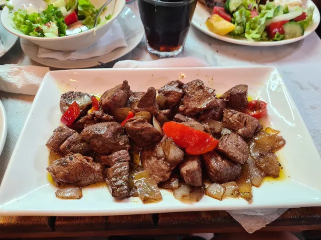 Roasted beef cubes with onion and red pepper on a white plate, with green salad in the background