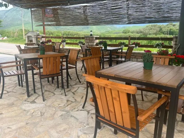 A terrace covered with matting with wooden tables, flower pots and a view of green hills