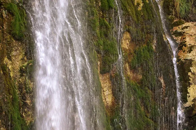 A white waterfall running down a rock wall covered in green moss
